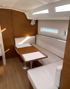 Un intérieur compact avec une table et un banc en bois, un petit ventilateur et une fenêtre laissant entrer la lumière naturelle.