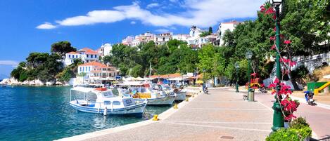 Une ville côtière où des bateaux sont amarrés, avec une promenade pavée et des bâtiments aux toits rouges.