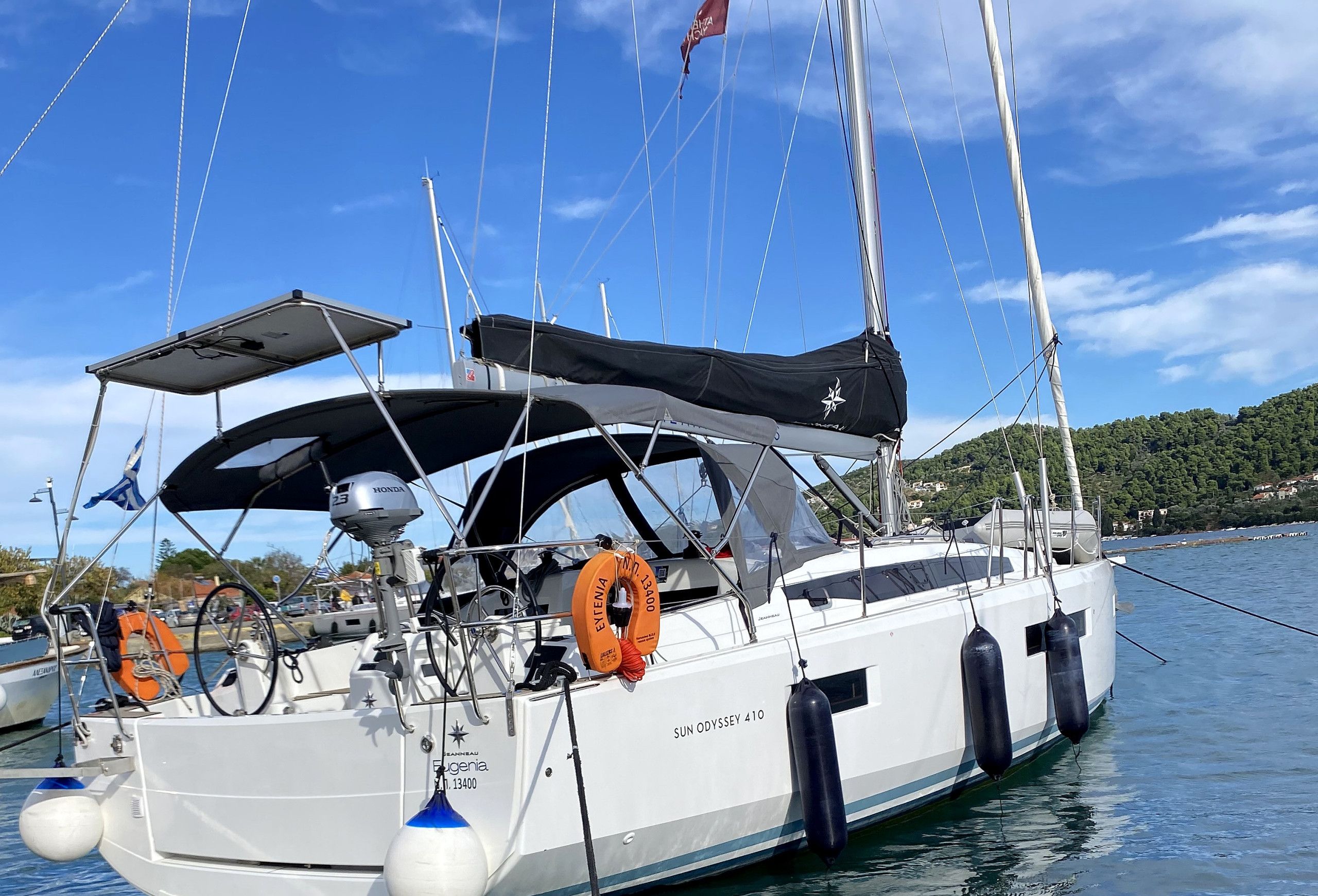 A sailboat docked at a marina with a clear sky, a lifebuoy, and a Honda outboard motor.