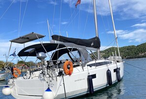 Un voilier est amarré dans une marina, sous un ciel dégagé. On peut y voir une bouée de sauvetage et un moteur hors-bord Honda.