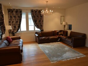 A living room with a brown leather sofa, a large rug, and a chandelier. - Haus am Bach Appartement/Fewo, Dusche oder Bad, WC 8-Bettwohnung by Interhome (Zweisimmen)