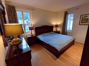 Quarto com cama de madeira, duas mesas de cabeceira com lumin árias, uma janela com cortinas e um quadro na parede.