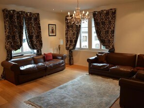 A living room with two leather sofas, a chandelier, patterned curtains, and a rug. - Haus am Bach Appartement/Fewo, Dusche oder Bad, WC 8-Bettwohnung by Interhome (Zweisimmen)