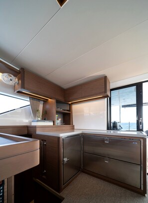 A modern kitchen with stainless steel appliances, wooden cabinetry, and a large window offering a view of the sea.