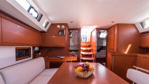 Interior de barco com mesa de jantar, assentos acolchoados, painel de controle e cesta de frutas.