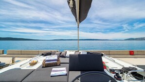 A boat deck with a cushioned seating area, a steering wheel, and a view of the water. - Sun-Kissed Sailing Adventure in Split, Croatia (Kaštel Gomilica)