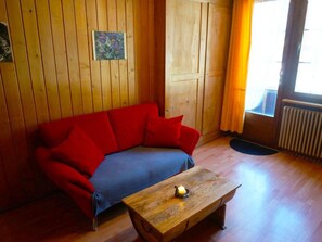A wooden-paneled room with a red sofa, a blue blanket, and a wooden coffee table with a candle. - Beatrice Appartement/Fewo, Dusche oder Bad, WC 3-Bettwohnung by Interhome (Zweisimmen)