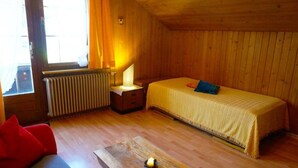 Une pièce comprenant un lit, une petite table, un radiateur et une fenêtre avec des rideaux.