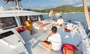 Eine Yacht mit Sonnendeck, Sitzgelegenheiten und Blick auf Wasser und Hügel im Hintergrund.
