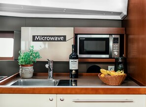 A kitchen with a microwave, a sink, a potted plant, a bottle of wine, and a basket of fruit.