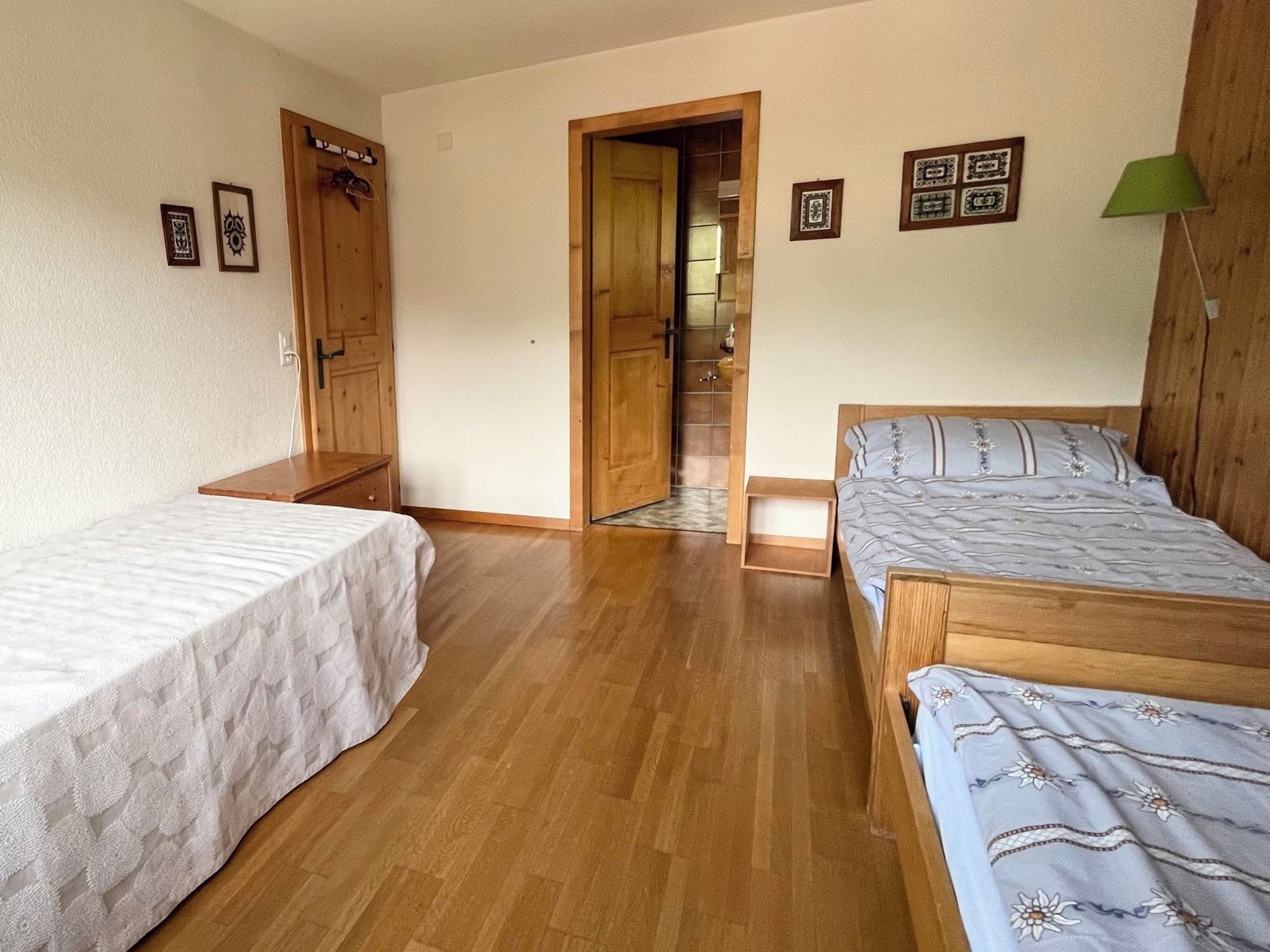 Una habitación con dos camas, suelo de madera, una puerta que da a un baño y una lámpara verde.