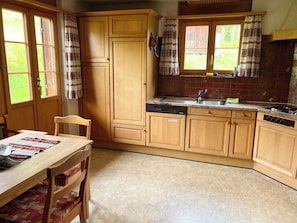 A kitchen with wooden cabinets, a sink, and a dining area with a table and chairs. - Akelei (gross) Appartement/Fewo, Dusche oder Bad, WC 7-Bettwohnung by Interhome (Zweisimmen)