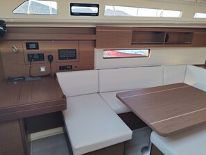 Schiffsinnenraum mit Holztisch, gepolsterten Sitzen, einer Armaturenkonsole und Fenstern.