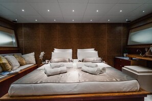 A large bed with white linens and towels, a wooden bench with cushions, a small bedside table, and a large mirror.