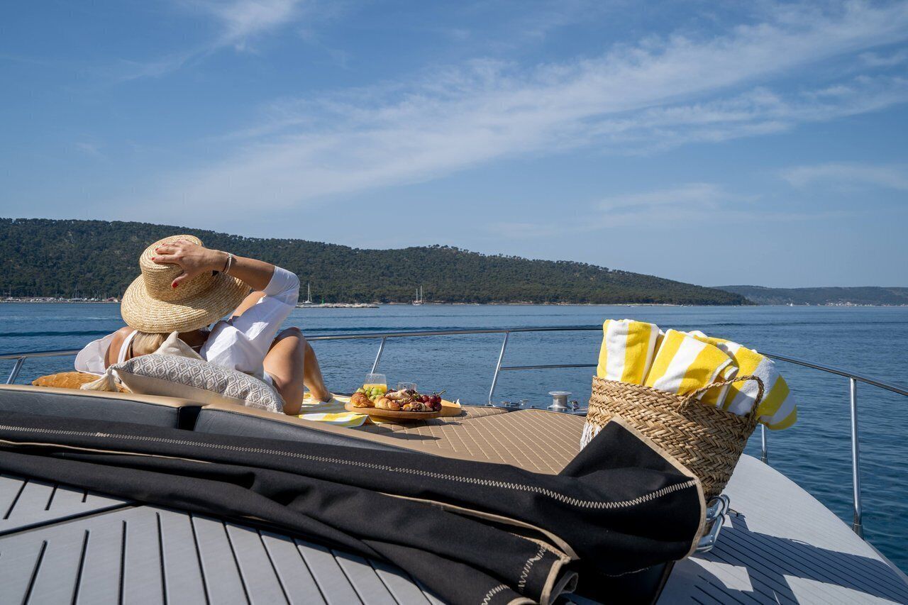 A person relaxing on a boat with a hat, a basket, and a tray of food.