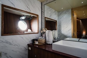 A bathroom with a large mirror, a round mirror, a bathtub, and a marble wall.