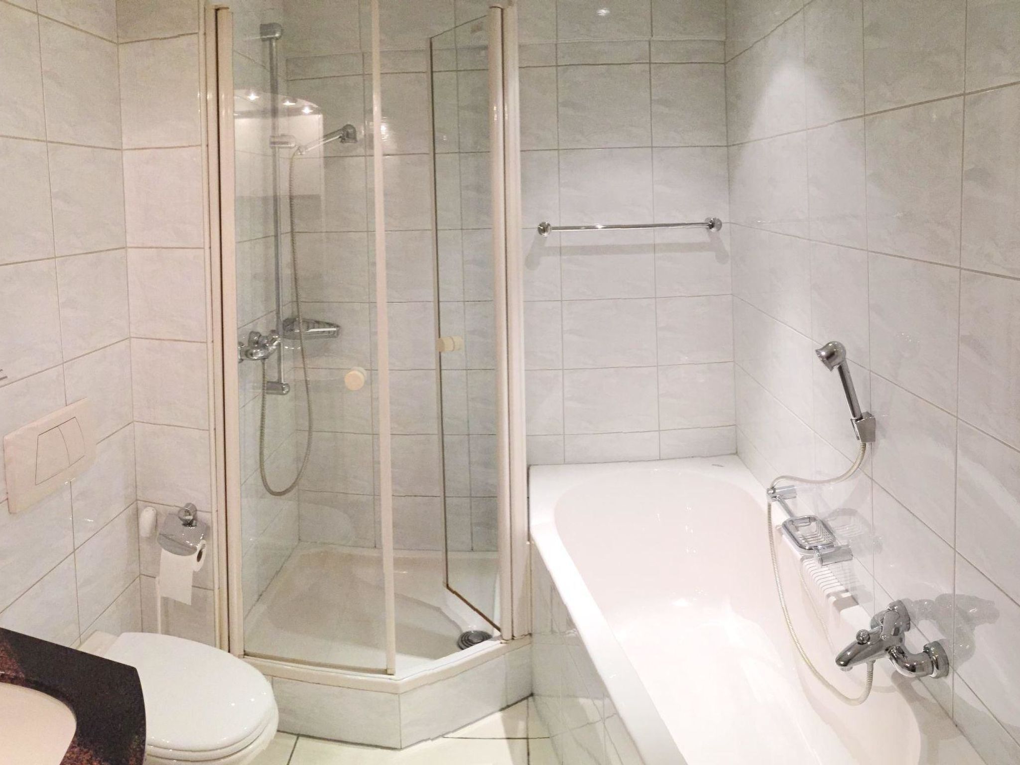 A bathroom with a glass-enclosed shower, a white bathtub, and a toilet.