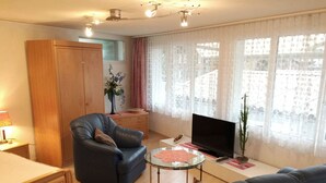 A living room with a sofa, a chair, a TV, a glass coffee table, and a wardrobe. - Studio Poli Studio, Dusche oder Bad, WC 2-Bettwohnung by Interhome (Zweisimmen)