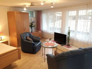 A living room with a sofa, a chair, a TV, a glass coffee table, and a wardrobe. - Studio Poli Studio, Dusche oder Bad, WC 2-Bettwohnung by Interhome (Zweisimmen)