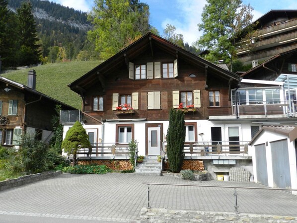 Un edificio de estilo chalé tradicional con fachada de madera, varias ventanas con contraventanas y un balcón con jardineras.