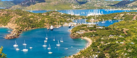Une zone côtière où de nombreux voiliers sont amarrés dans une marina, le tout étant entouré d’une végétation luxuriante et de collines.