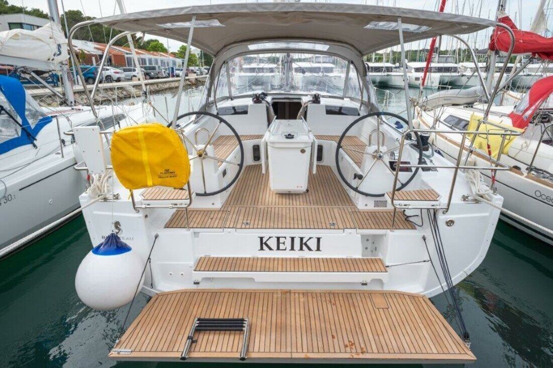 Eine Yacht namens KEIKI liegt in einer Marina mit Holzdeck, Steuerrad und Rettungsboje vor Anker.