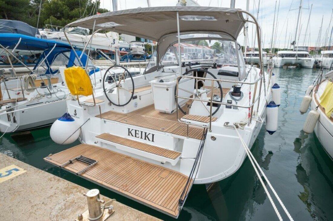 A white yacht named KEIKI docked at a marina with multiple boats, a wooden deck, and a covered seating area.
