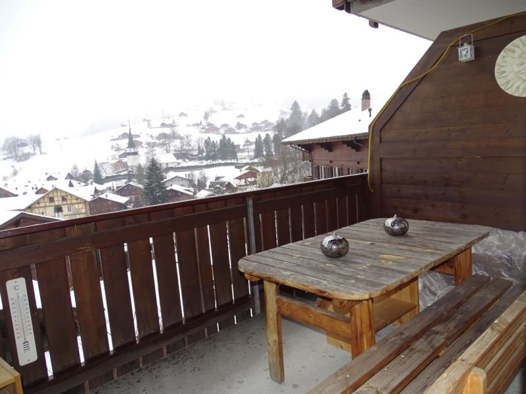 A wooden deck with a table and bench, overlooking a snowy village.