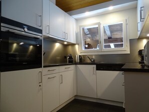 A modern kitchen with white cabinets, a black countertop, and a window above the sink. - Kristall Appartement/Fewo, Dusche oder Bad, WC 6-Bettwohnung by Interhome (Zweisimmen)