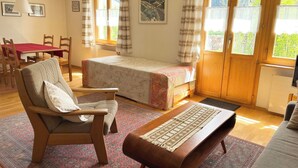 Ein gemütliches Zimmer mit Bett, Sessel, Tisch und einem Vorhangfenster.