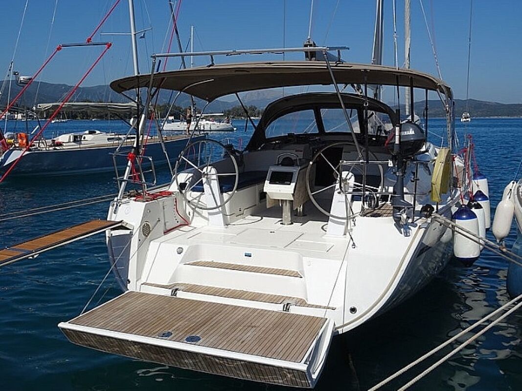 Un velero amarrado en una marina, con cubierta de madera, timón y toldo.