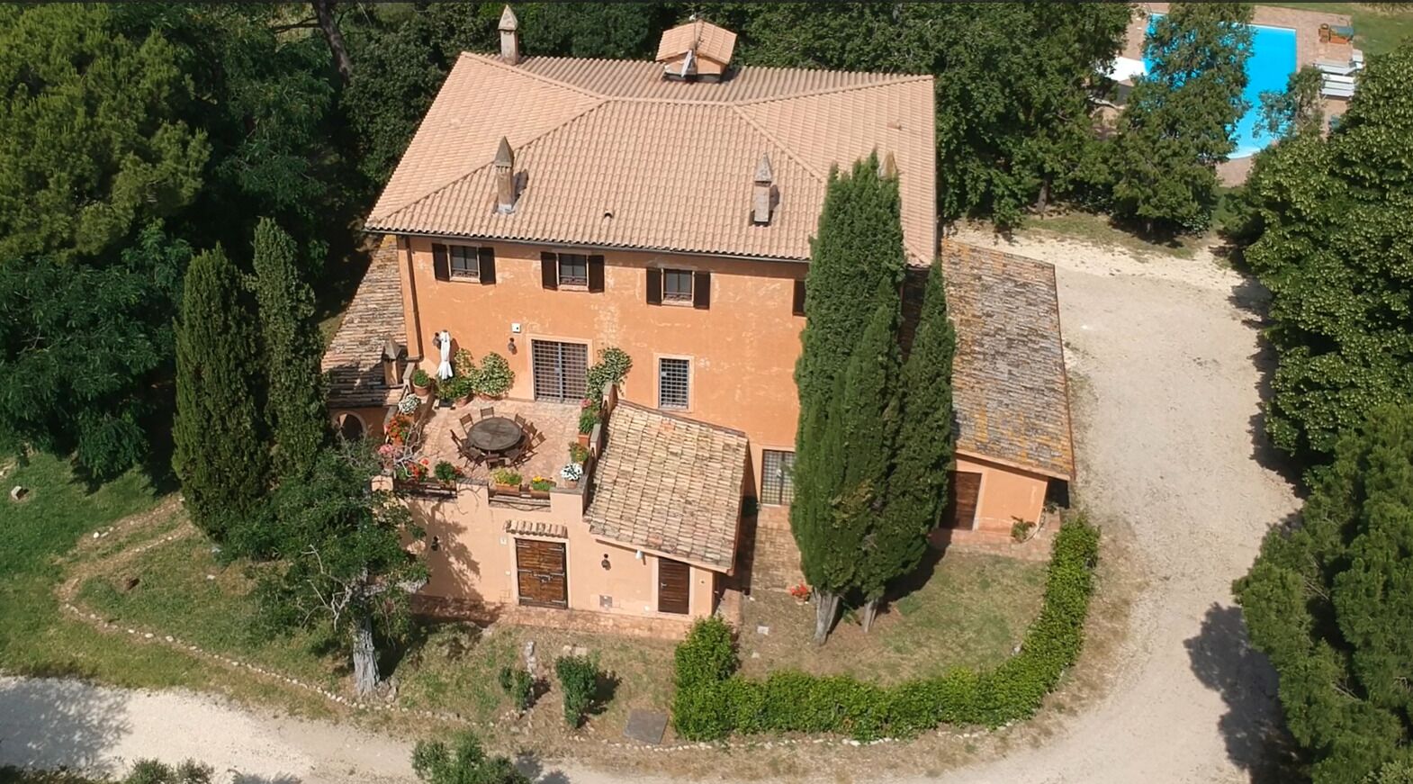 An aerial view of a two-story house with a tiled roof, surrounded by greenery and a swimming pool.