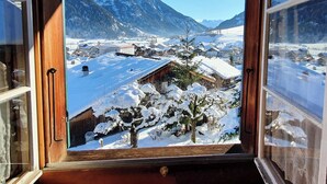Aussicht aus dem Fenster auf ein verschneites Dorf mit Bergen im Hintergrund.
