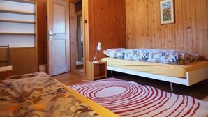 Ein Zimmer mit Holzwänden, einem Bett, einem Schreibtisch und einer Tür zu einem weiteren Raum.