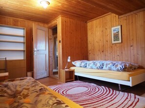 Ein Zimmer mit Holzwänden, einem Bett, einem Schreibtisch und einer Tür zu einem weiteren Raum.
