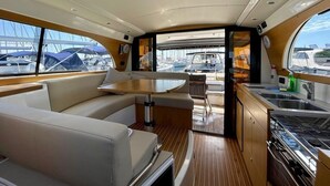 En yachtinteriør med spiseplads, et køkken og udsigt til lystbådehavnen.