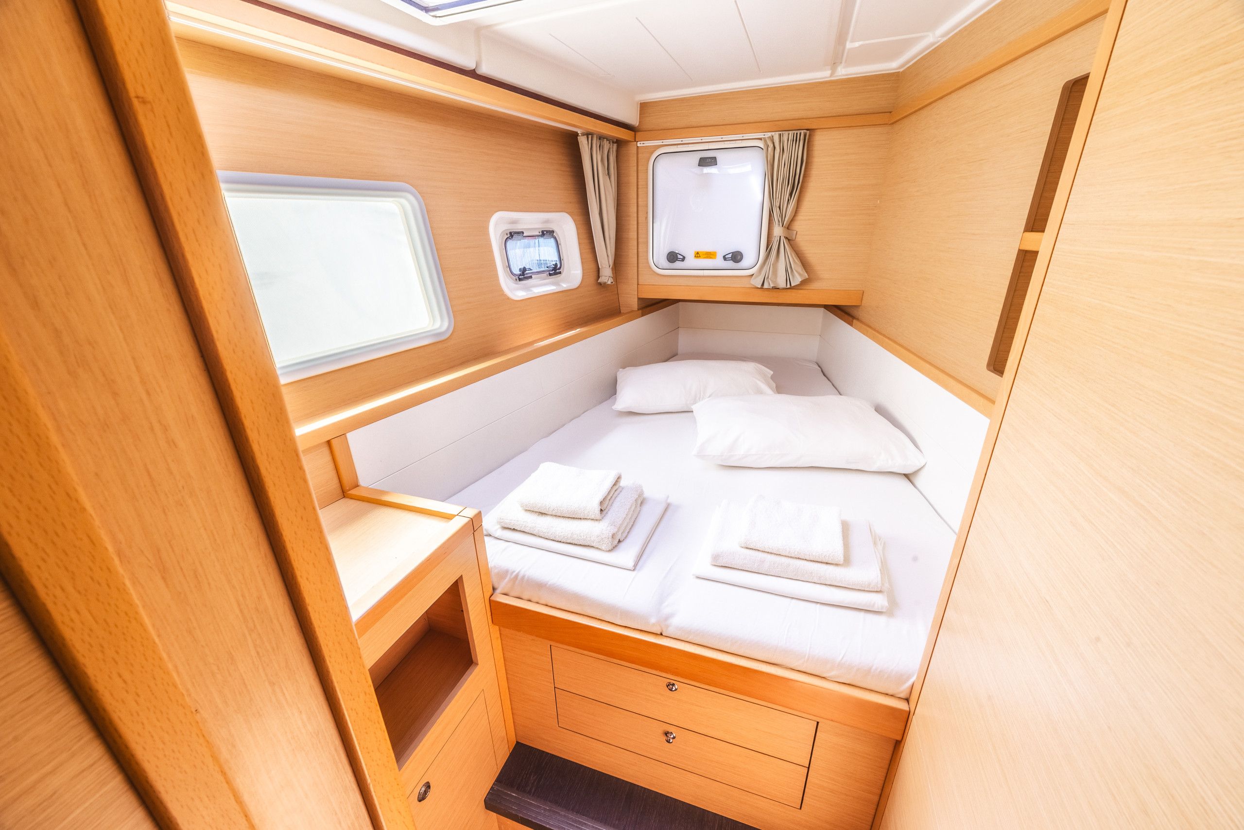 Ein kleines, helles Schlafzimmer mit Bett, zwei Fenstern, einem kleinen Tisch und einem Stauraumschrank.