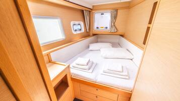 Une chambre à coucher de taille modeste, bien éclairée, comprenant un lit, deux fenêtres, une petite table et un meuble de rangement.