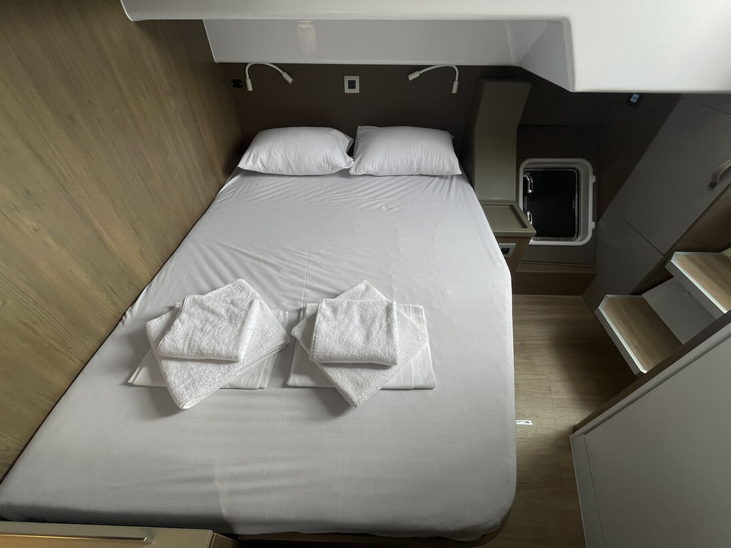 Ein ordentlich bezogenes Bett mit weißen Laken, ein kleiner Nachttisch und ein Fenster.