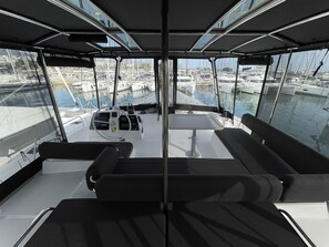 A boat's deck with a steering wheel, a table, and seating. - Sun-Kissed Sailing Adventure in Islas Sarónicas (Alimos)