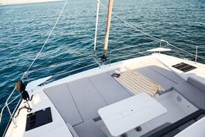 Cubierta de barco con una mesa blanca, asientos acolchados y vista al agua.