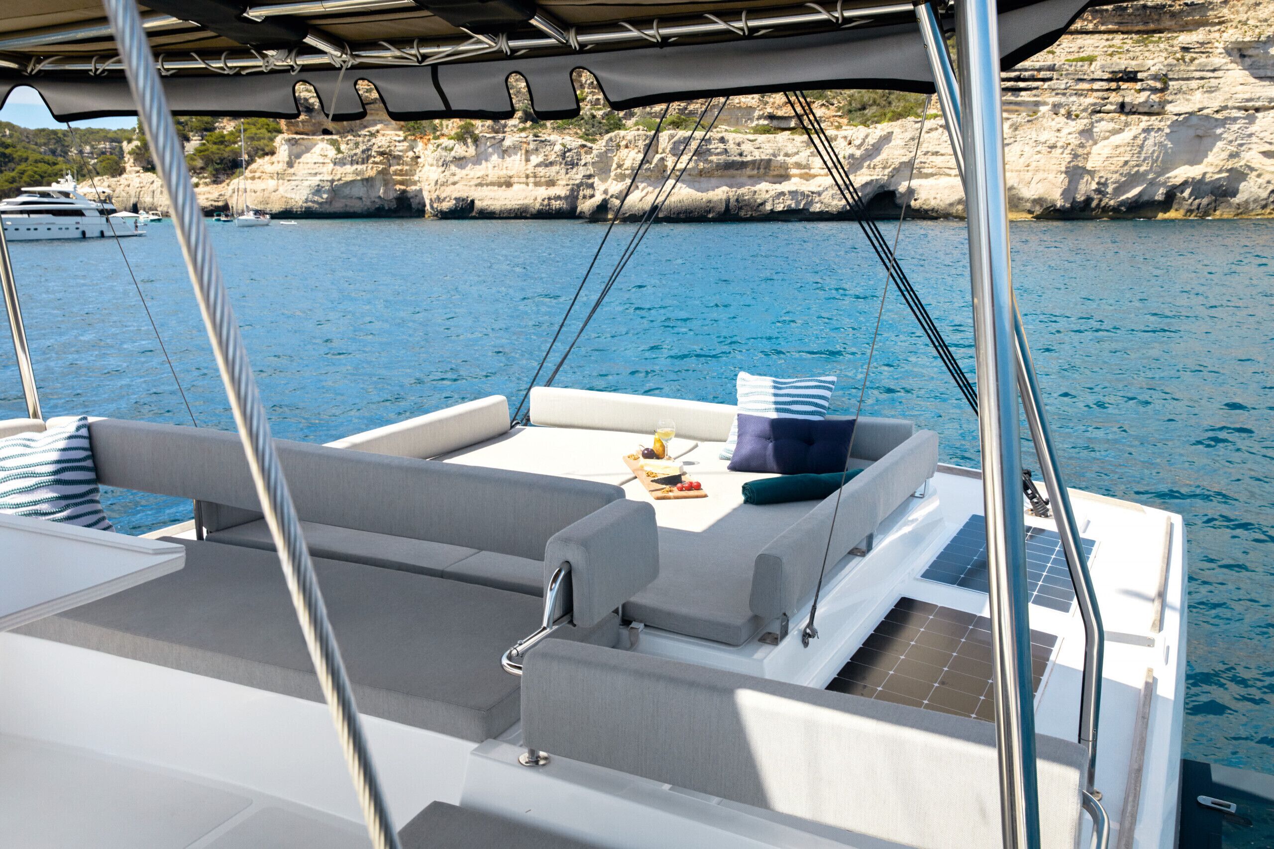 Ein Bootsdeck mit Sitzgelegenheiten, einem Tisch mit einem Getränk und Blick auf Wasser und Klippen.