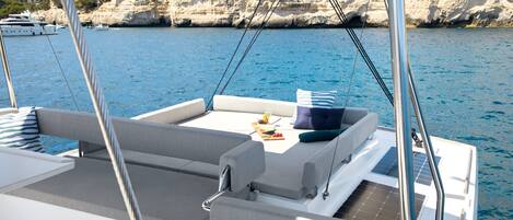Ein Bootsdeck mit Sitzgelegenheiten, einem Tisch mit einem Getränk und Blick auf Wasser und Klippen.