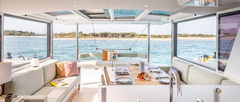 Un intérieur de bateau moderne comprenant un coin repas, des sièges et une cuisine avec un évier.
