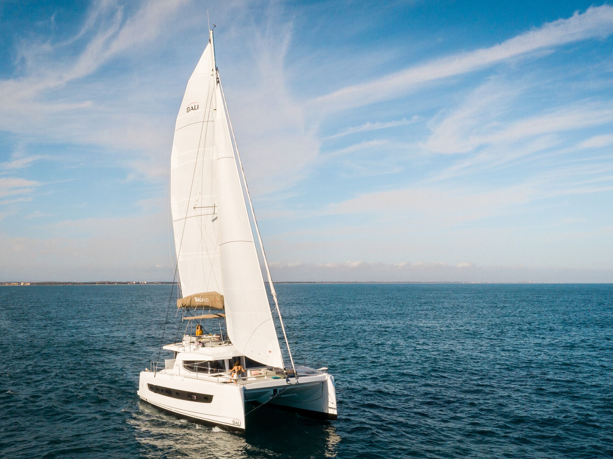 Un voilier à la coque blanche et à la grande voile blanche, naviguant sur une mer calme.