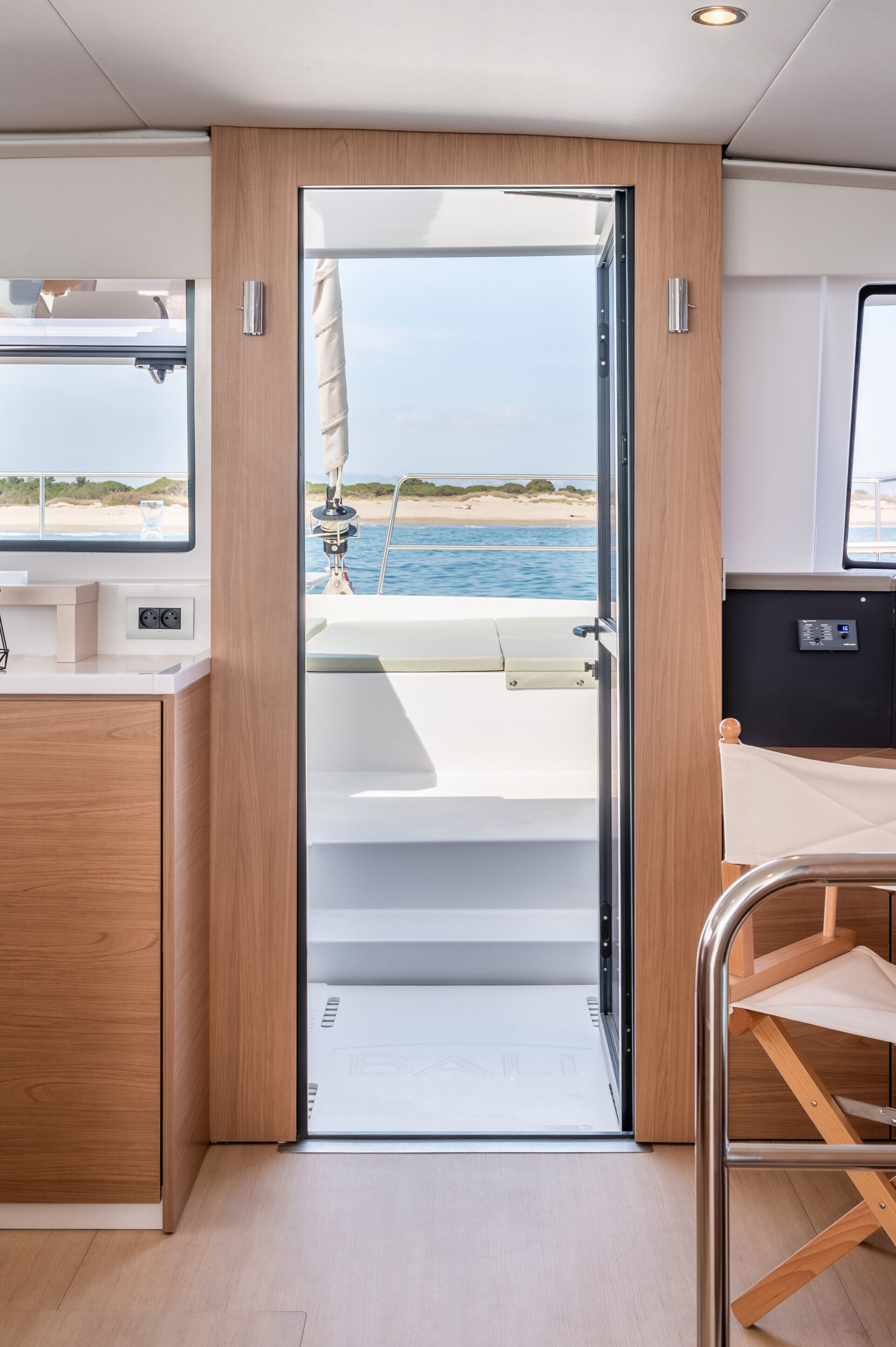 Un intérieur moderne avec une porte en bois donnant sur un espace extérieur, une petite cuisine et un coin salon avec vue sur la mer.