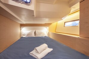 Eine schmale Kabine mit einem Einzelbett, Holzwänden und einem kleinen Fenster, auf dem Bett liegt ein zusammengerolltes Handtuch.