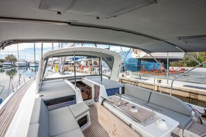 A boat's deck with seating, a small table, and a view of the marina. - Sun-Kissed Sailing Adventure in Islas Cícladas, Mykonos (Mykonos)