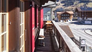 Un balcone in legno con vista su una montagna innevata e una strada.