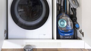 Una lavanderia funzionale con una lavatrice LG ThinQ ad carica frontale e un aspirapolvere Philips.